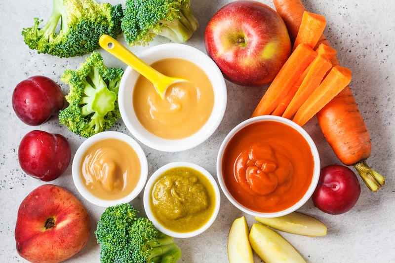 Vegetable and fruit baby puree (apple, broccoli, carrot, plum) in white bowl with ingredients following heavy metal compliance